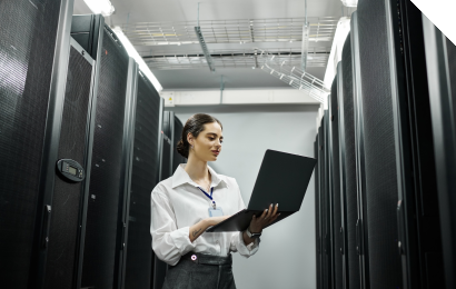 Person steht in einem Rechenzentrum zwischen Serverracks und hält einen Laptop in der Hand