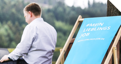 Ein Mitarbeiter von OC sitzt, an seinem PC arbeitend, draußen auf einer Bank im Headquarter von OPITZ CONSULTING in Nochen.  