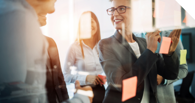 Eine Frau klebt Haftnotizen an eine Glaswand und spricht mit einem Mann
