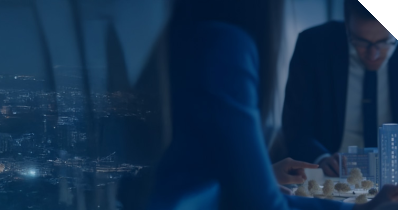 Personen sitzen um einen Tisch auf dem modellhaft einige Hochhäuser aufgebaut ist. Im Hintergrund befindet sich eine Großstadt. 