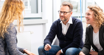 Eine Bewerberin sitzt in einer Interviewsituation zwei Mitarbeitenden gegenüber. 